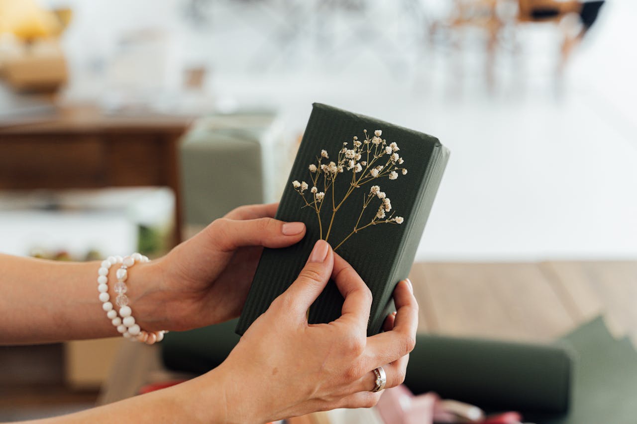 Close-up of hands holding a beautifully wrapped gift with floral accents, ideal for special occasions.