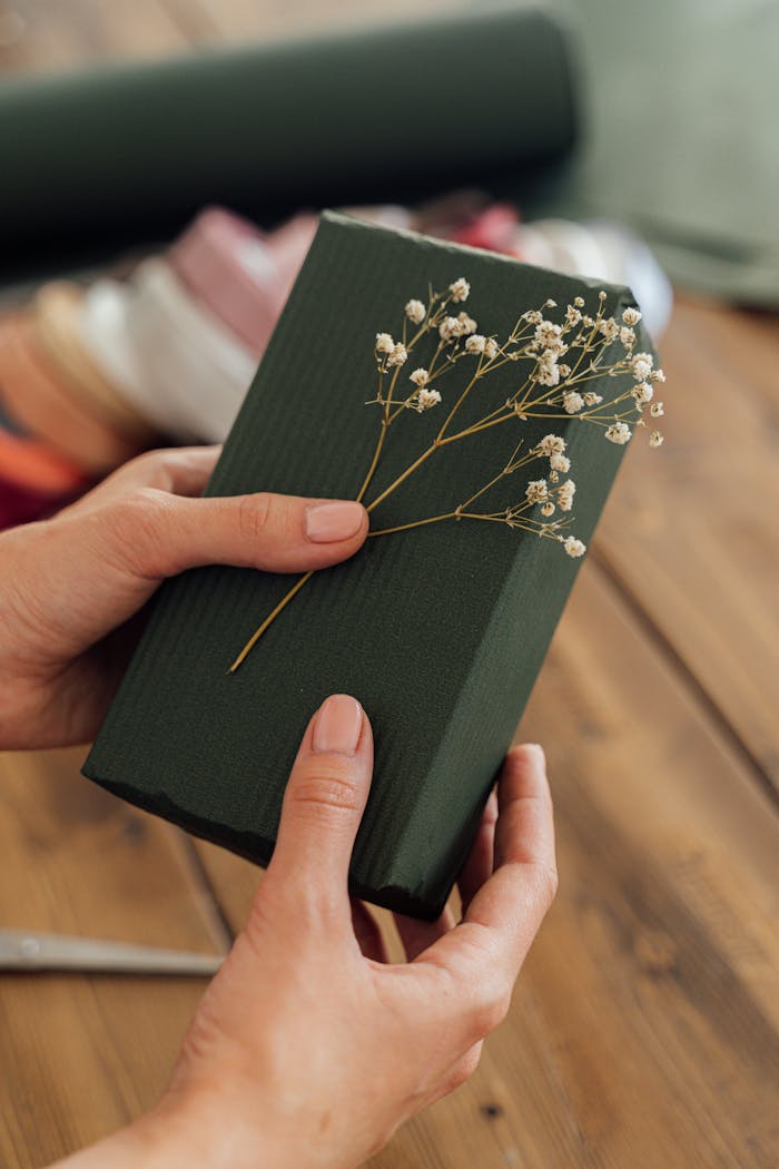 A close-up of hands holding a beautifully wrapped green gift adorned with delicate flowers.